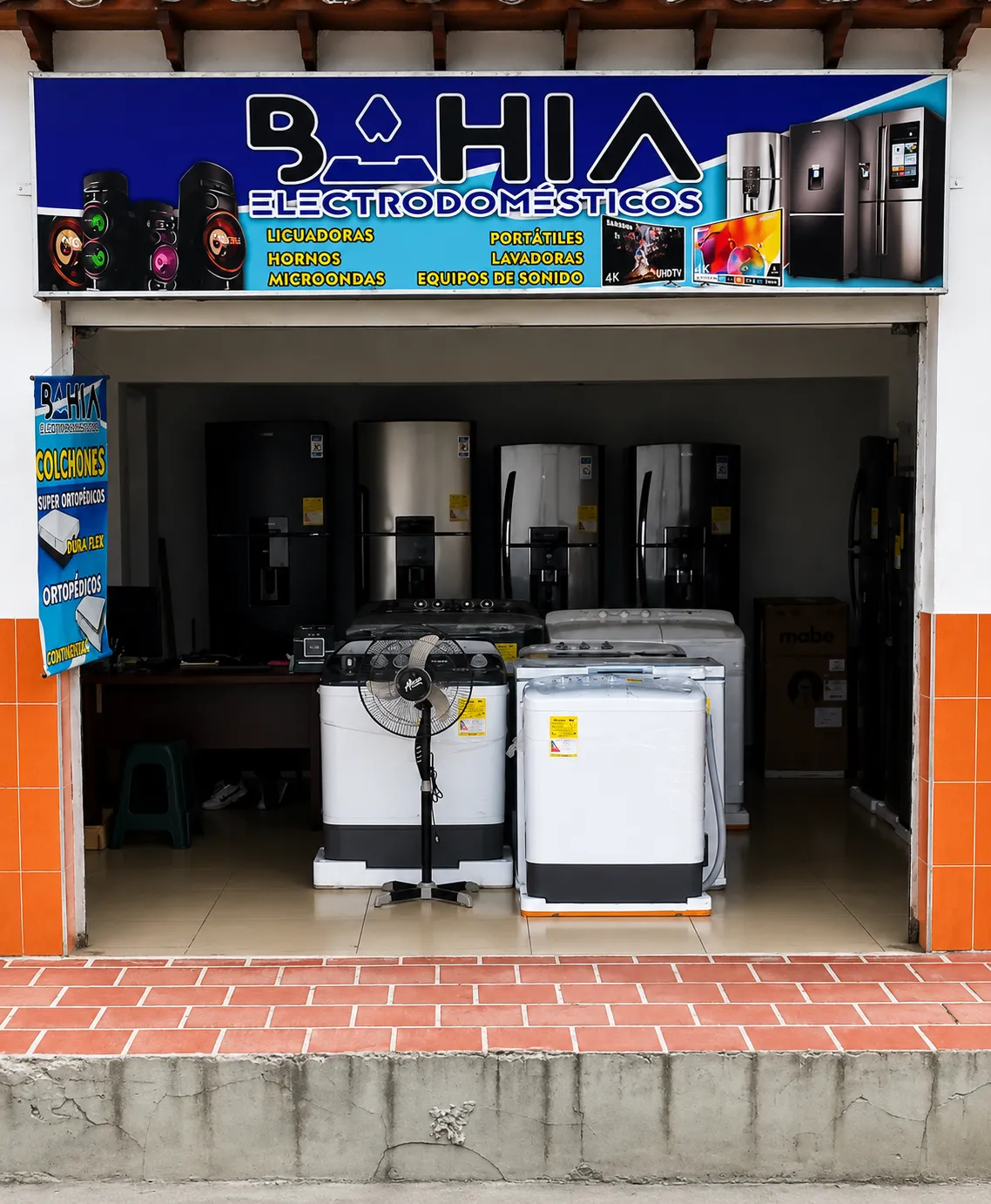 Fachada del almacén Bahía Electrodomésticos en Ábrego: aviso azul con el nombre del negocio y, a la entrada, neveras, lavadoras y una estufa.